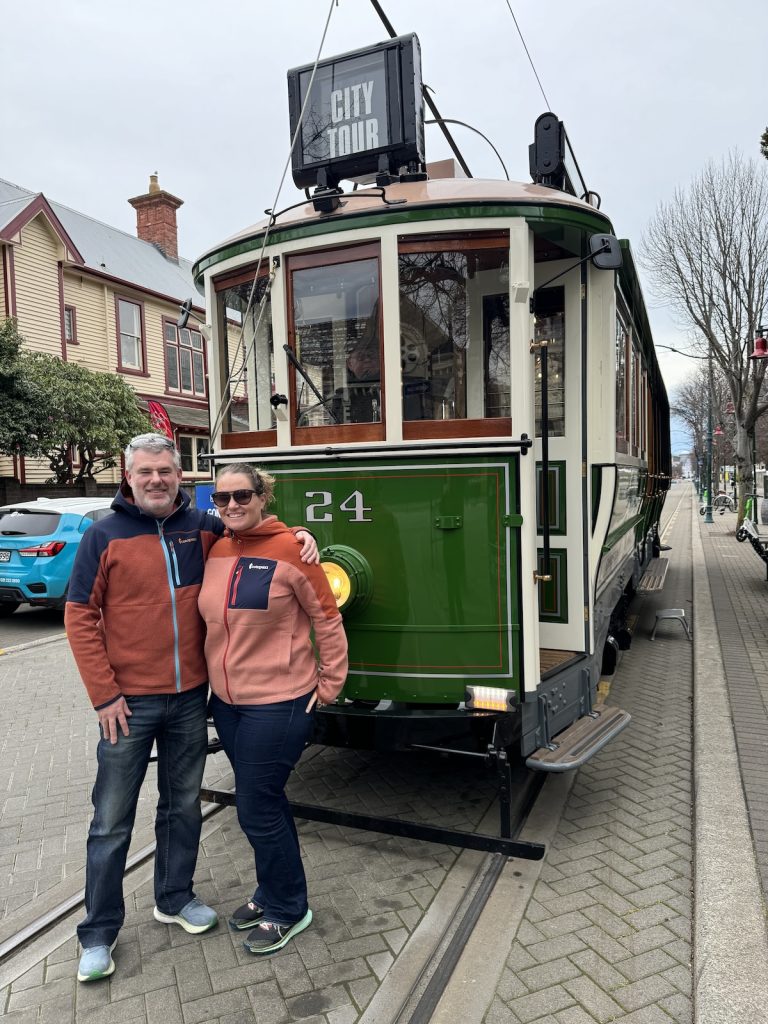 Couple posing in front of green and white City Tour tram on brick street.