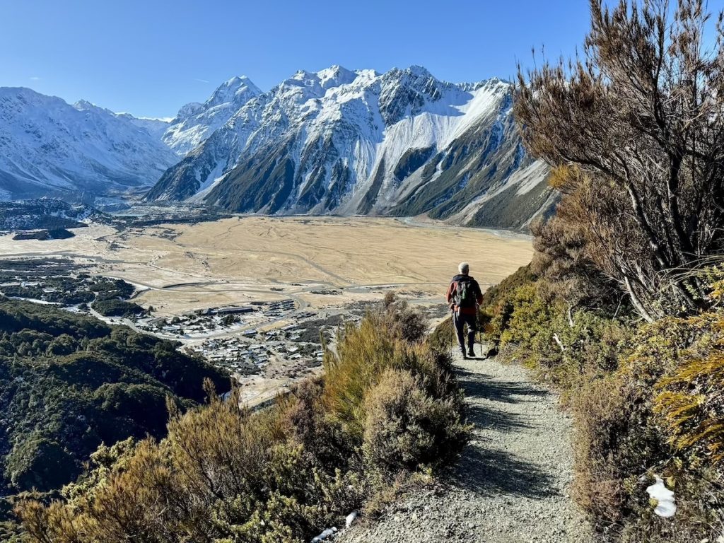 Hiker on a trail overlooking a valley and snow-capped mountains.